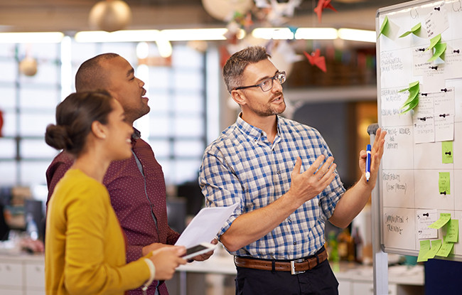 Trois collègues en train de discuter tout en regardant un tableau blanc