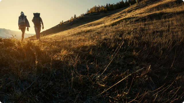 pair of hikers walking trail as sun is setting