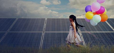 A girl running beside a solar grid holding a bunch of balloons in her hand