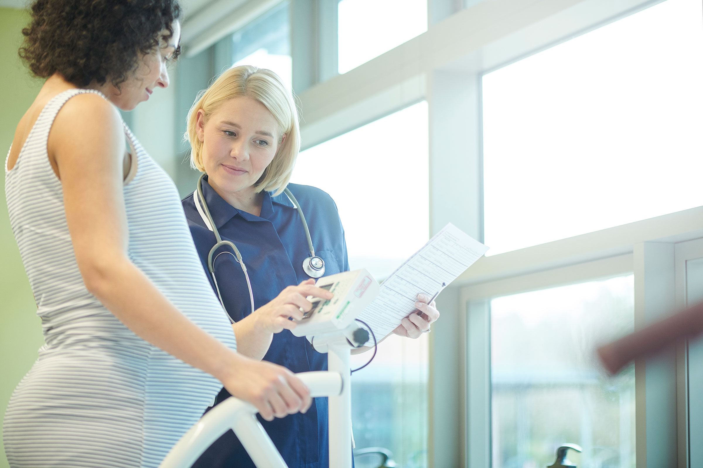 A pregnant person, left, speaks with a doctor, right, while she points at a clipboard. 