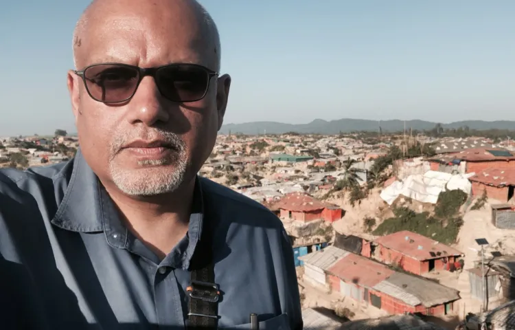 A man in a blue shirt takes a selfie in front of houses.