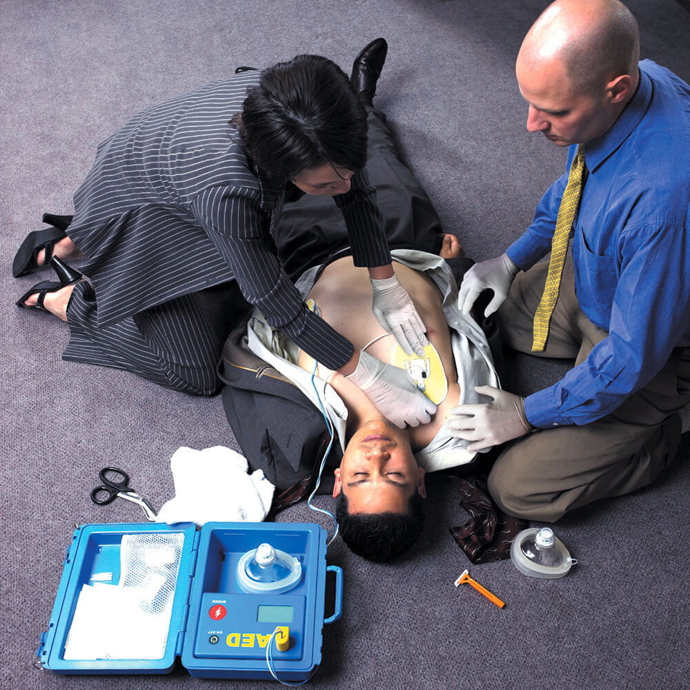 business woman using AED on man on office floor with male assistant image