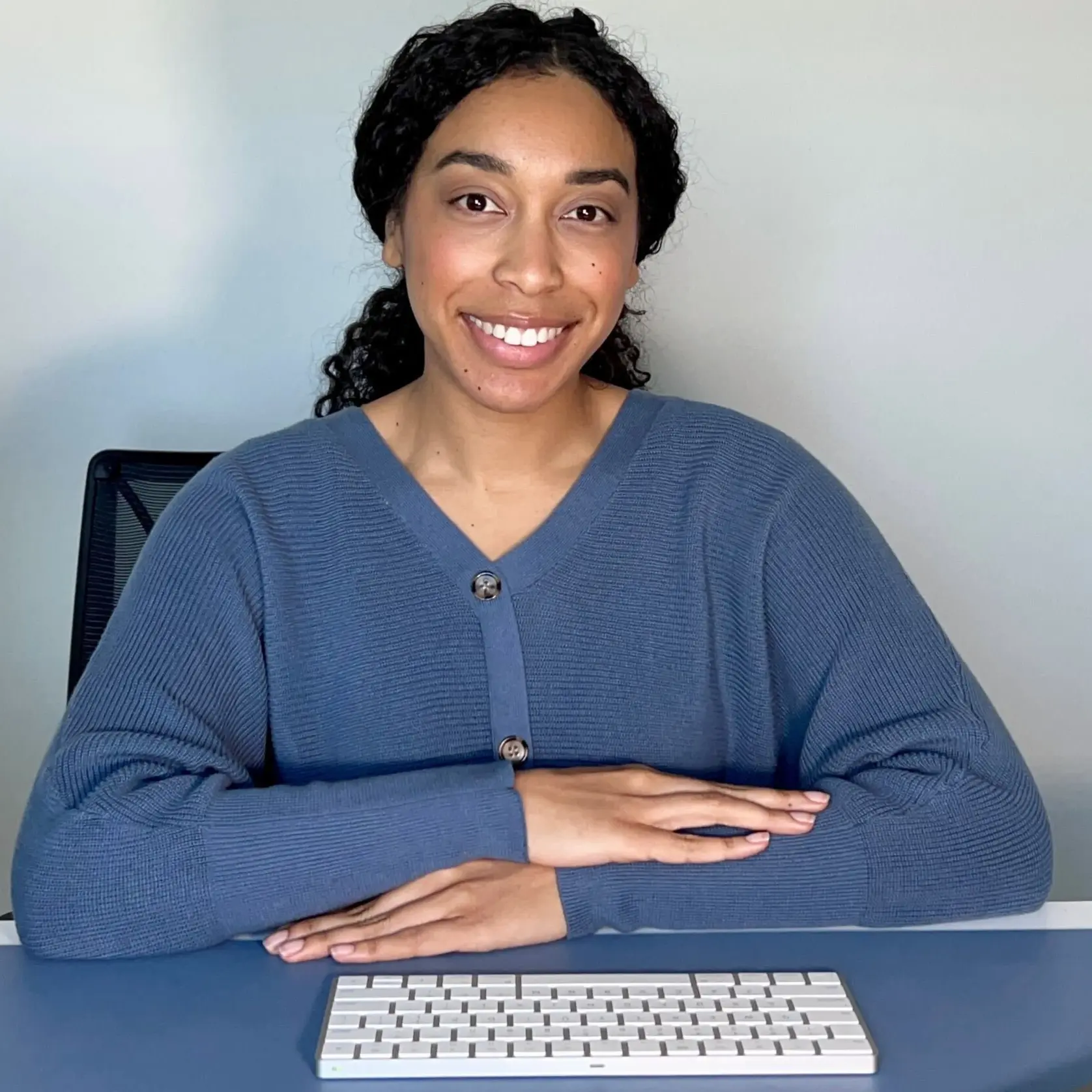 A picture of Gabrielle Woody, who is wearing a blue shirt and smiling in front of a desk with keyboard