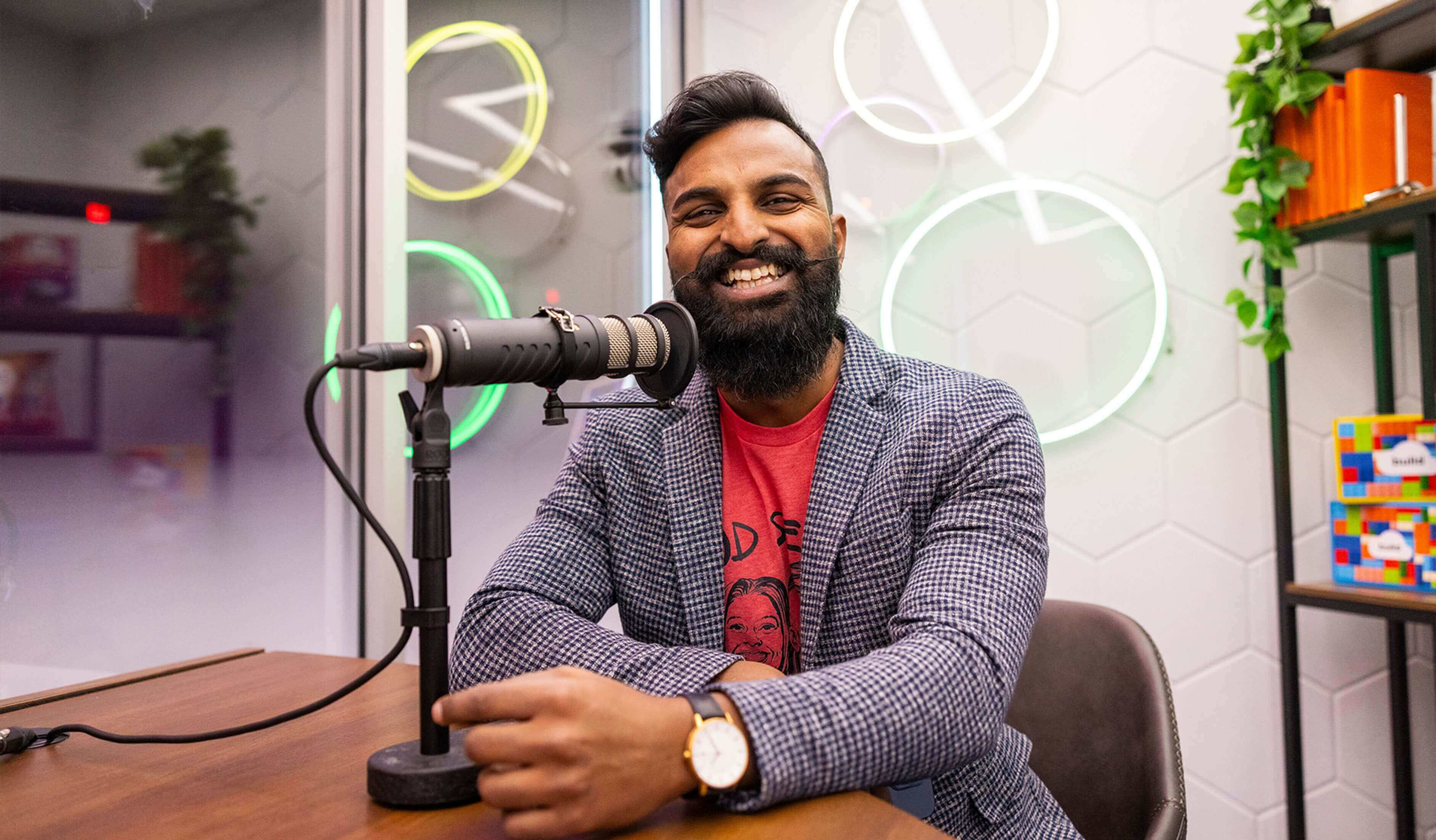 men looking smiling at camera with microphone in front of him in recording studio