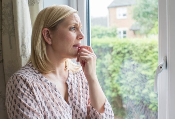 A worried woman looking out of the window.