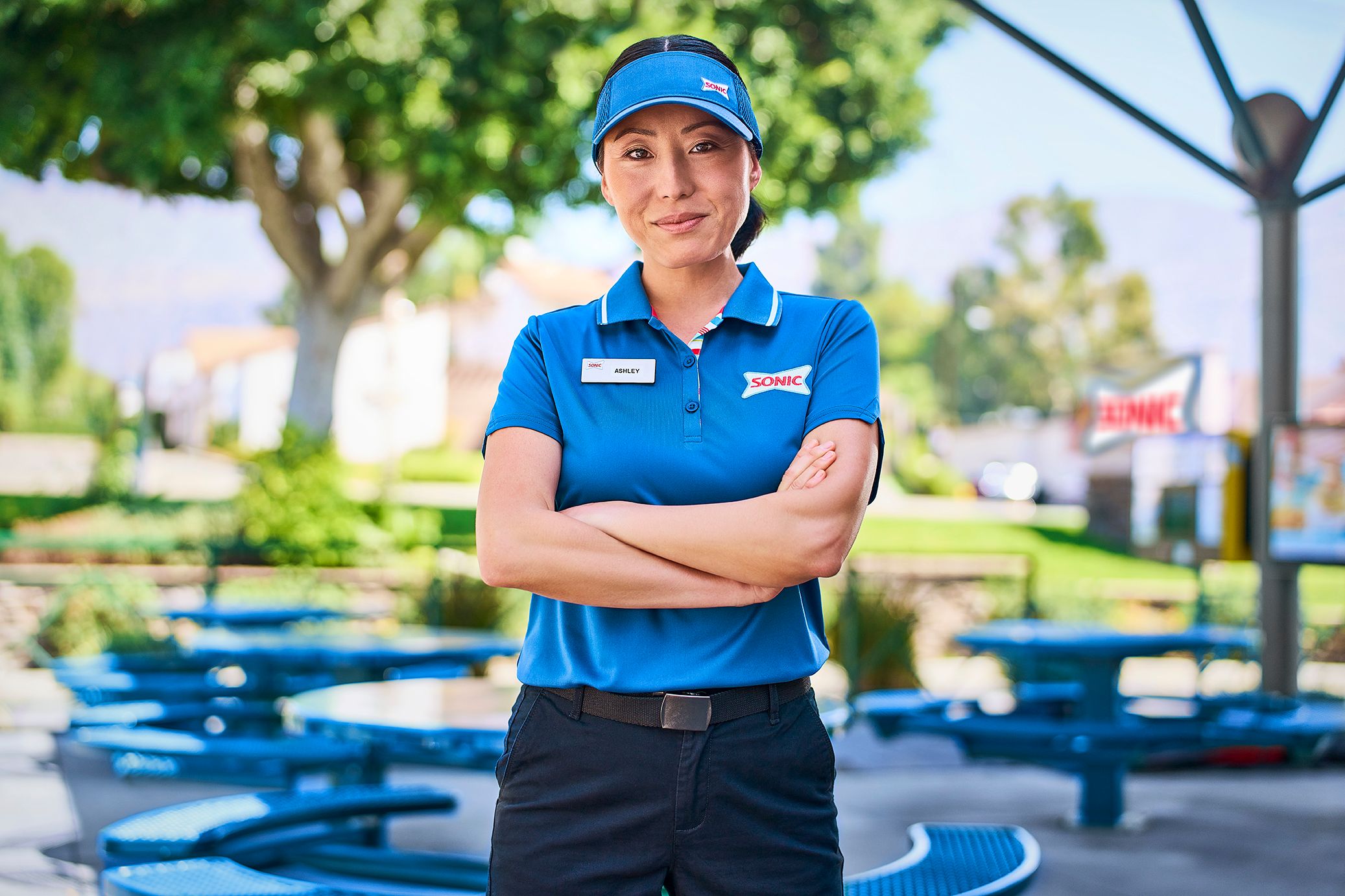 Confident Sonic employee with arms crossed in an outdoor seating area.