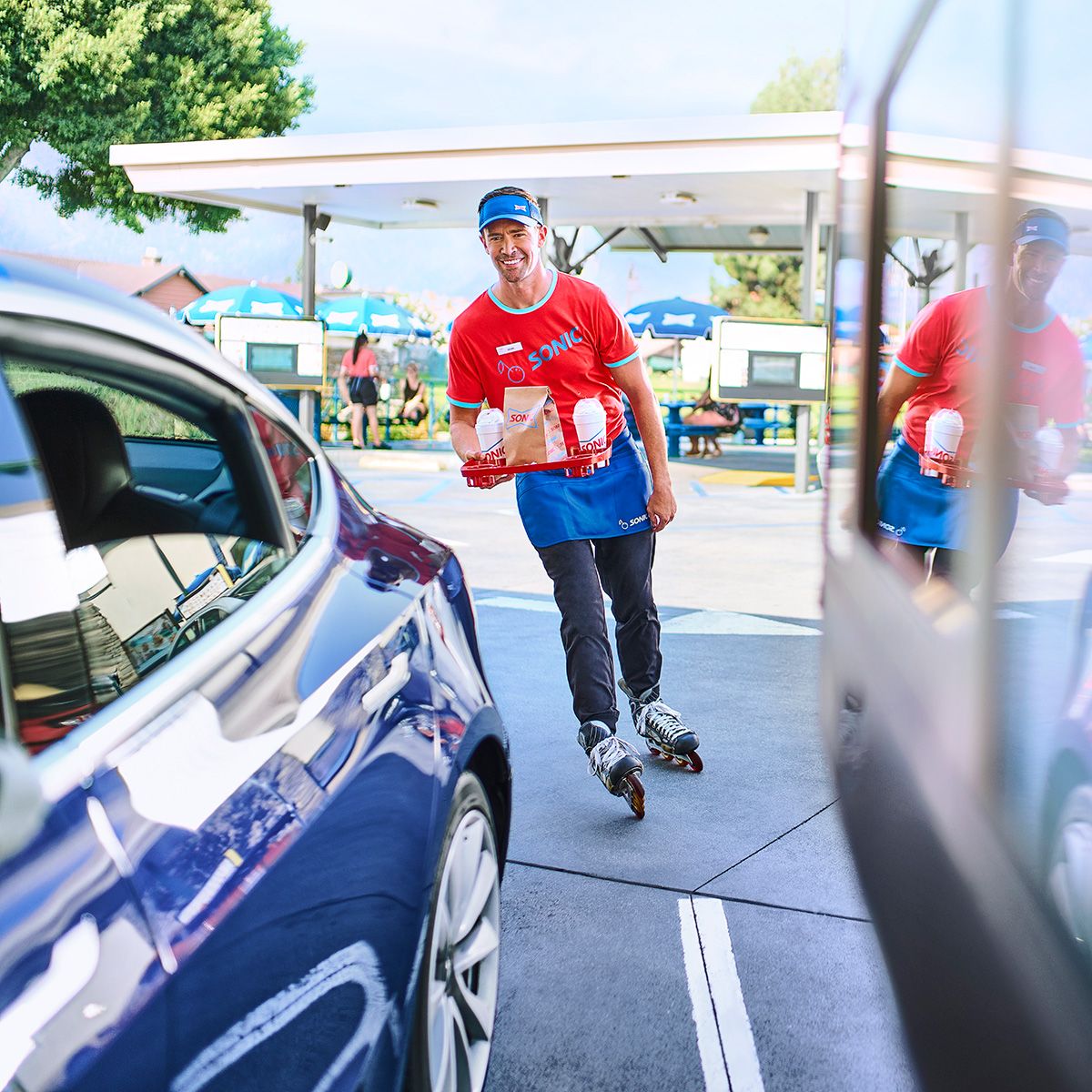 Sonic employee on roller skates delivering an order to a car.