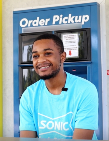 Employee in a blue shirt at Sonic Order Pickup station, smiling