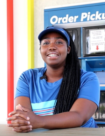 Smiling employee in blue uniform at Order Pickup station