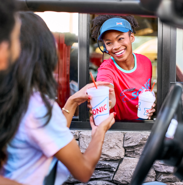 Drive-thru employee handing drinks to a customer with a smile