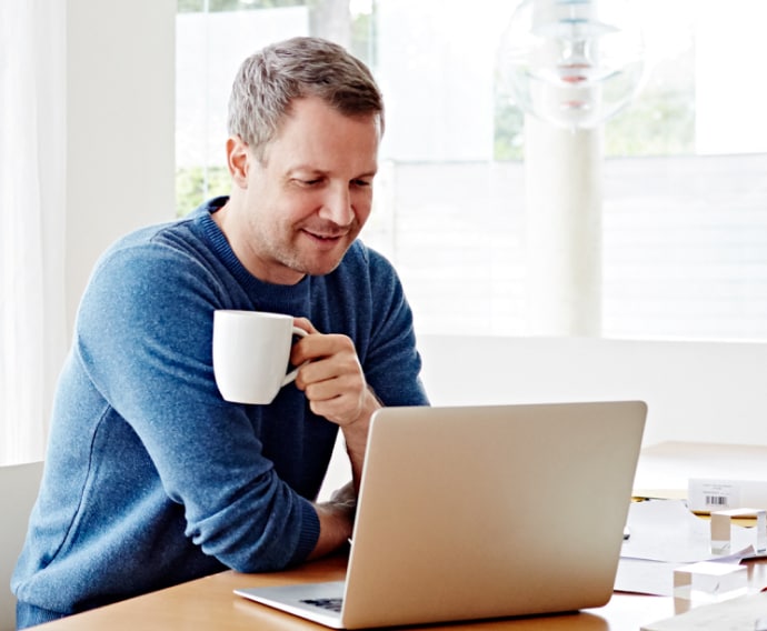 Mann zu Hause am Laptop, einen Kaffee trinkend.