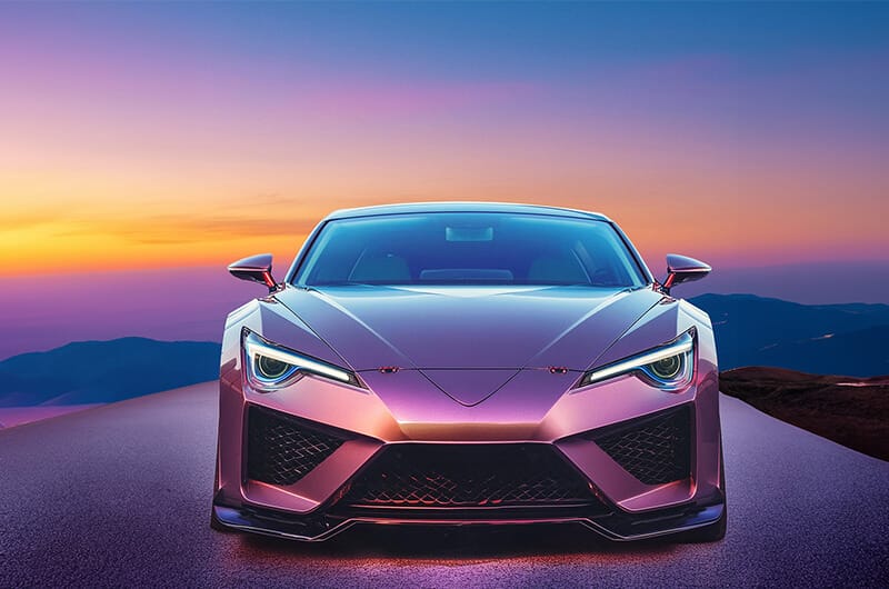 A sleek modern car with illuminated headlights is pictured front-facing on a road at dusk, with a colorful sunset and mountains in the background, symbolizing community innovation.