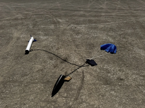 The blue, black, and white Fishhawk rocket after landing on the playa. The nose cone and airframe have separated and are connected by a black nylon recovery harness with a blue parachute connected to the harness.