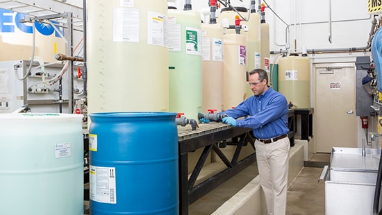 Man standing inside a commercial laundry working with laundry chemistry