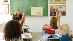 elementary students in classroom raising hands