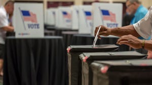 A person putting their ballot in a ballot box in front of a bunch of other voting booths