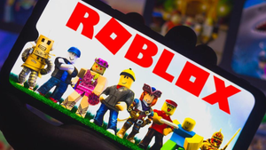 Roblox logo and various gaming characters displayed on a mobile device screen held in someone's hand