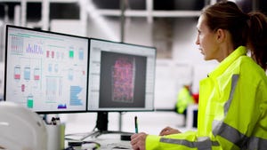 A woman in a reflective coat sitting at two computer screens