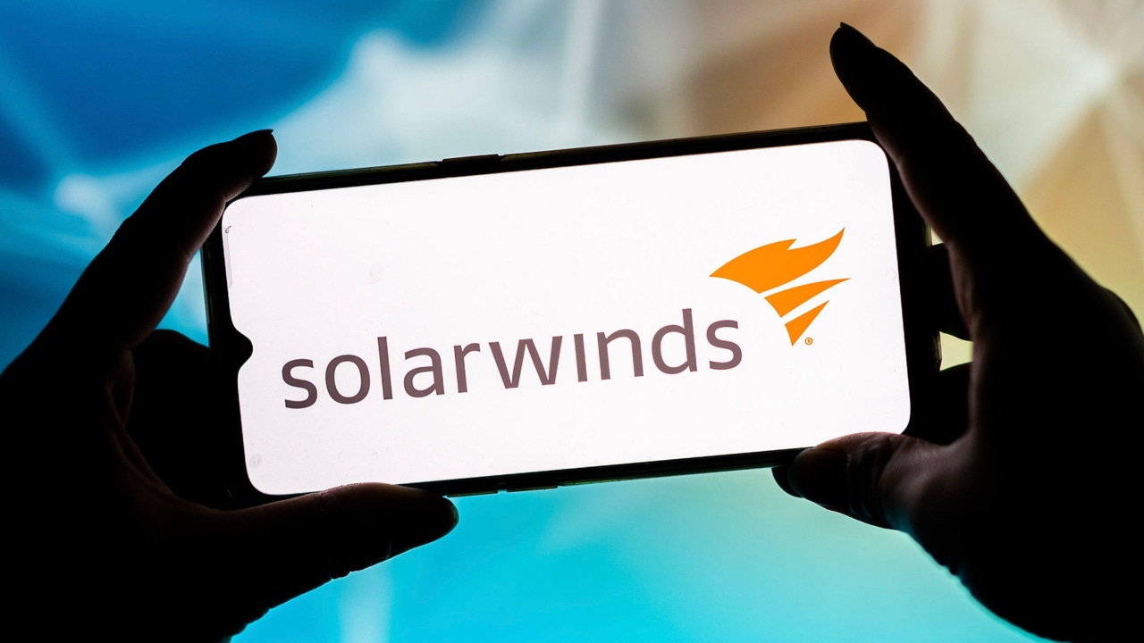 SolarWinds logo on a phone held up horizontally; background is blurred out