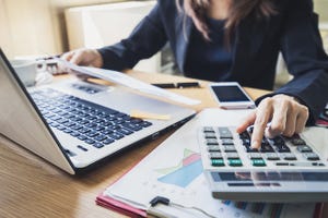 Businesswoman in a dark suit working at a desk with a calculator and financial paperwork.