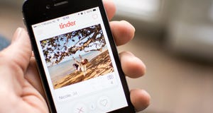 Mobile device in a hand with the Tinder app open to a profile