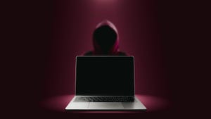 Shadowy hooded figure with an open laptop computer in the foreground