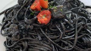 Black noodles on a platae topped with tomato