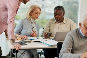 An older white woman and Black man learn and discuss the use of technology in a retraining course in the classroom.