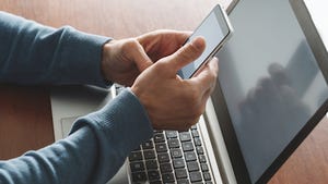 Multifactor authentication concept. A person is typing on smartphone in front of a laptop to help prevent social engineering. 