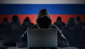 Hooded figures behind laptops in front of a background of the Russian flag