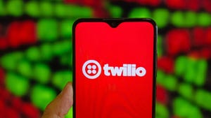 A person's hand holding a phone with the Twilio logo on the screen in white on a red background