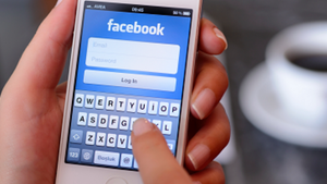 Hands holding a white mobile device showing the Facebook login page