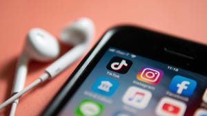 A close up of mobile screen with the TikTok app on display, with a pair of wired earbuds beside it