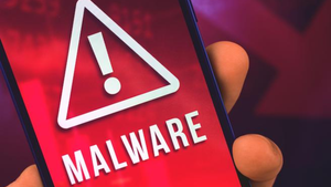 Mobile phone in someone's hand with the screen showing the word malware and a triangle with an exclamation point inside it