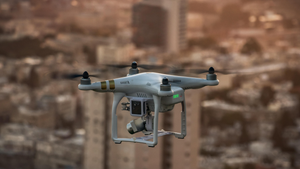 A gray drone device flying above a cityscape 