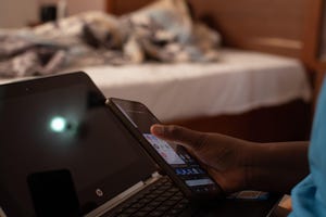 A woman holding a mobile phone in front of a laptop screen