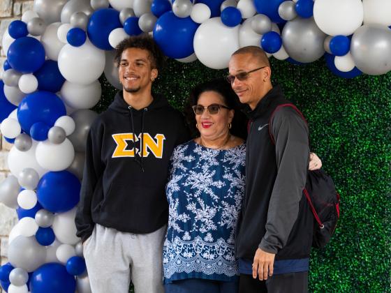 Family of three posing for a photo with a balloon arch behind them