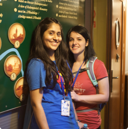 Two people standing in front of a notice board smiling while wearing conference badges