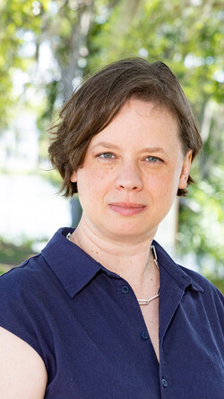 Headshot of Rachel Hooper in blue top against an exterior background of trees