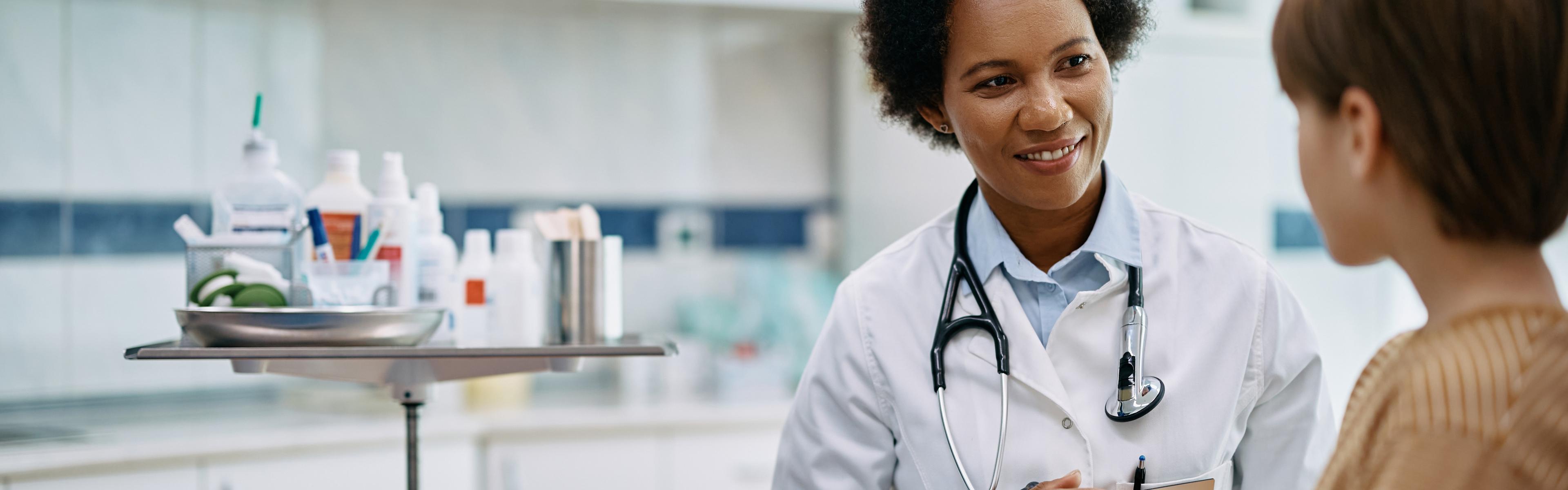 A female physician speaking with a juvenile male patient in a medical examining room.