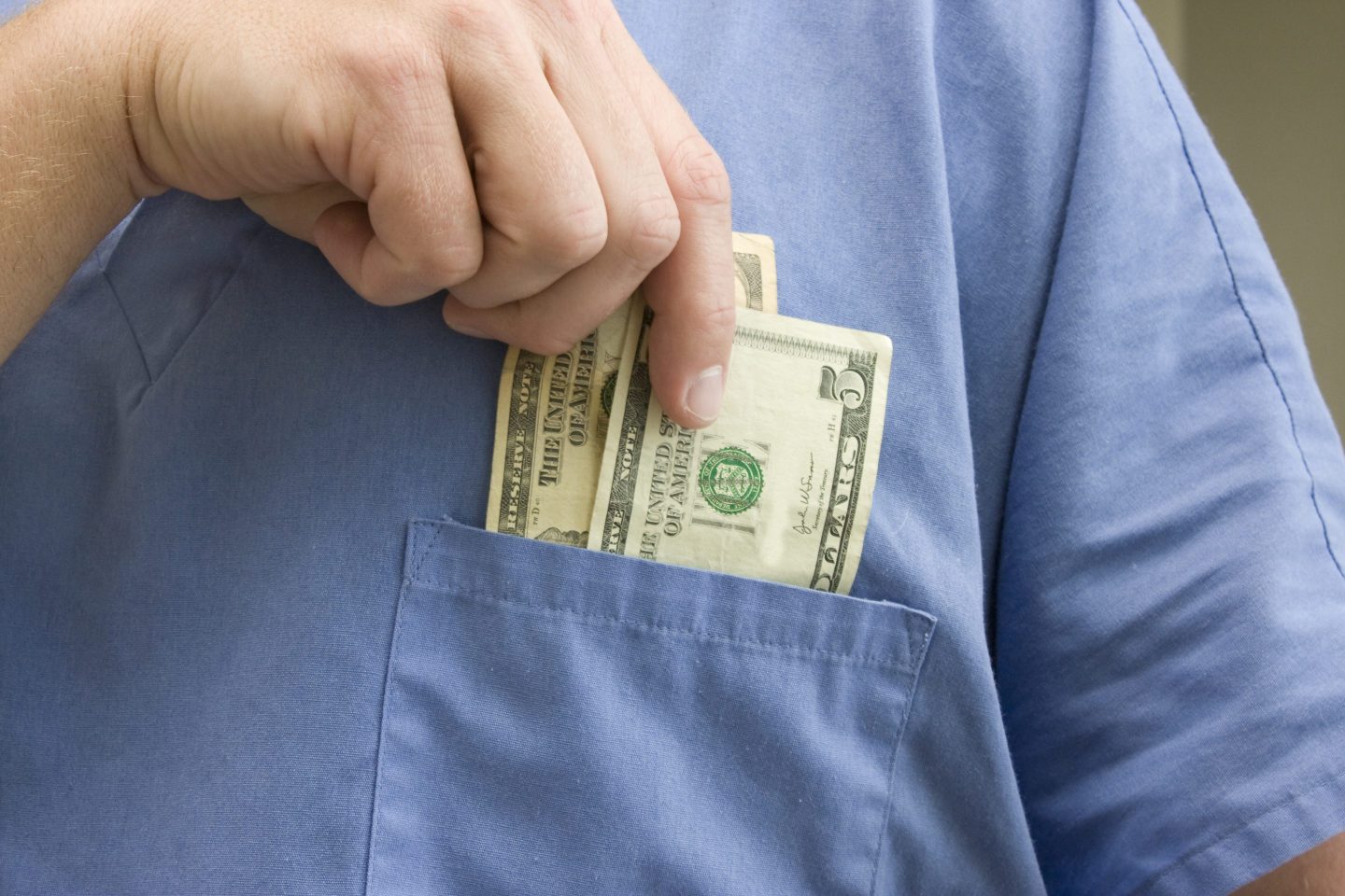 Nurse pulls cash out of the front pocket of their scrubs.