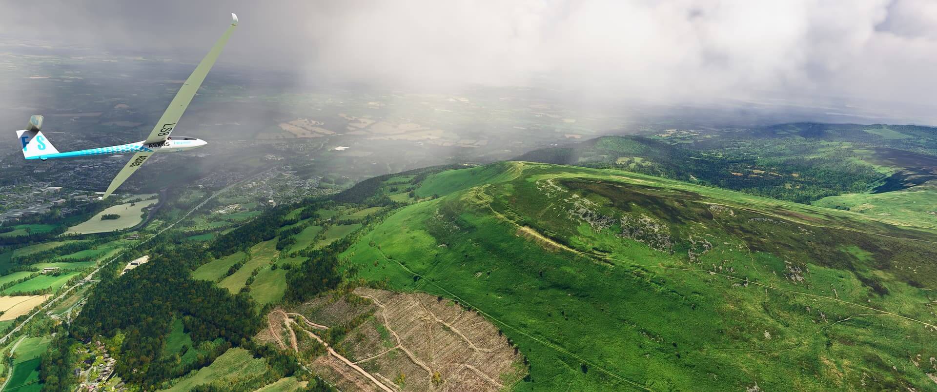 A glider in blue and white paint banks to the left to avoid rain whilst flying over green hills