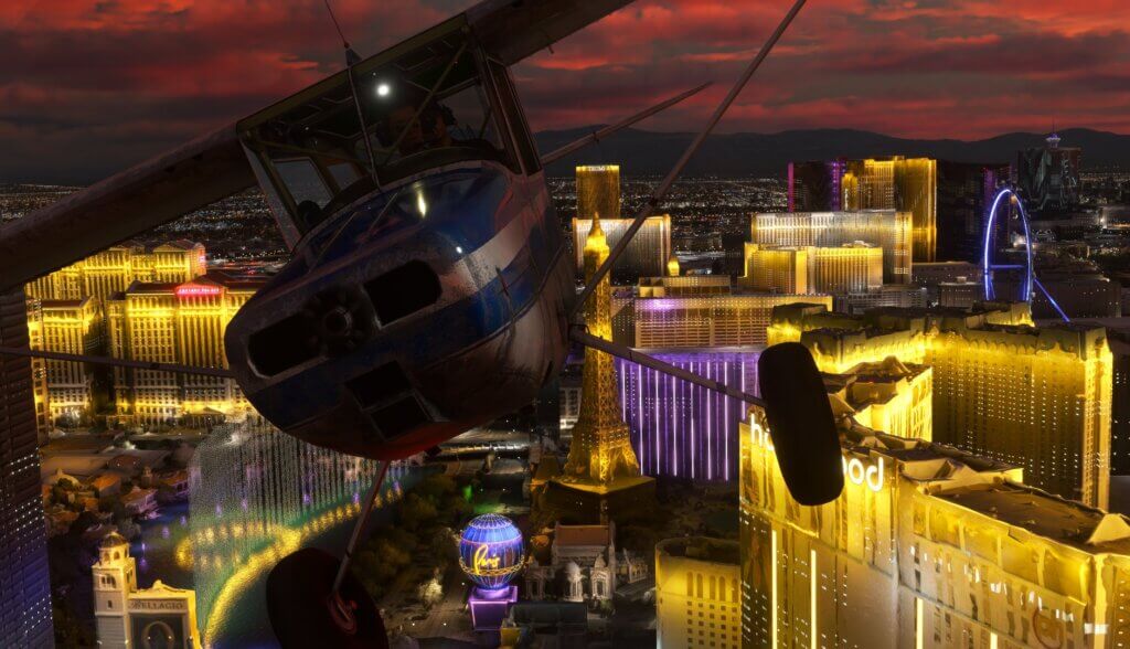 A Cessna 152 in blue and white paint flies down the Las Vegas strip at night with the Bellagio fountains spraying water behind