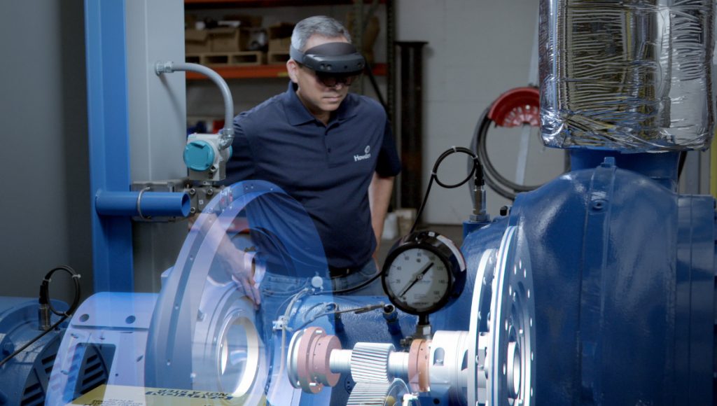 A worker oversees a piece of machinery with a digital model in extended reality through a headset.