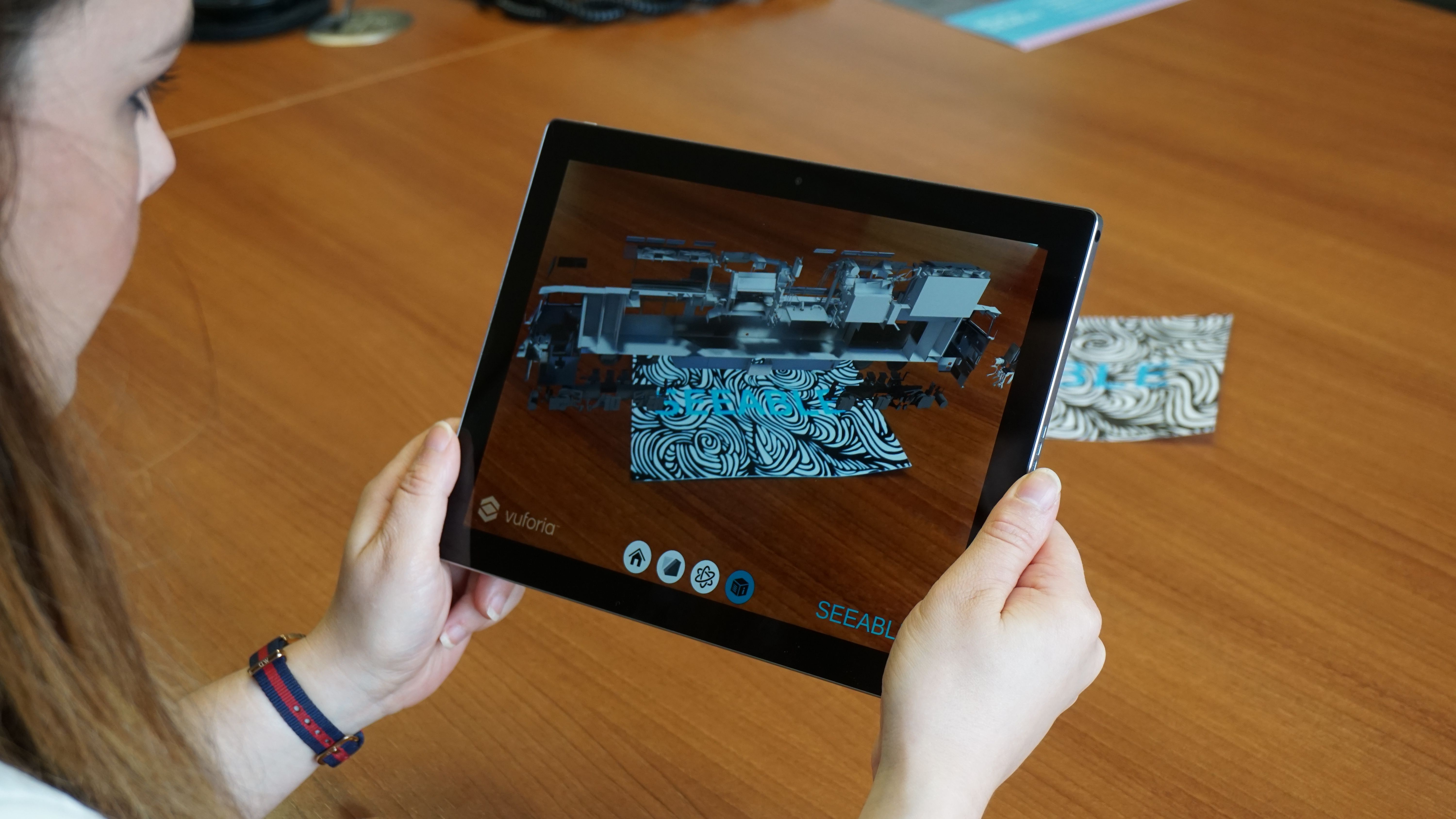 A person holding a tablet with an Augmented Reality application in view.