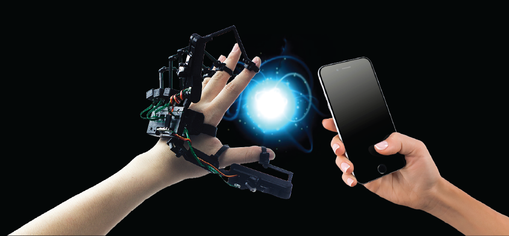 A hand wearing a graspable haptic device while another controls it with a phone.