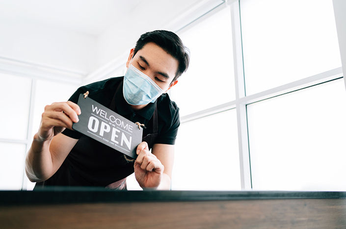 An asian man wearing a mask with a sign that says they're open