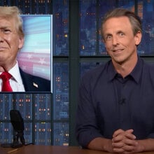 A man in a shirt sits behind a talk show desk. In the top-left is an image of Donald Trump.