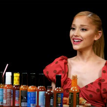 A woman sits in front of a table covered with hot sauce.