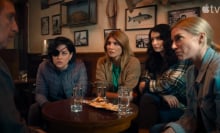 A group of women sit around a pub table looking at a man.